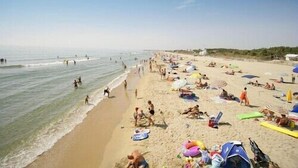 A crowded beach with people sunbathing and swimming, umbrellas, and beach chairs.