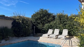 A swimming pool with two lounge chairs and a stone-tiled deck.