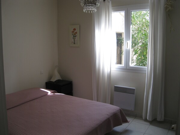 A bedroom with a bed, a radiator, a window with curtains, and a wall-mounted picture.