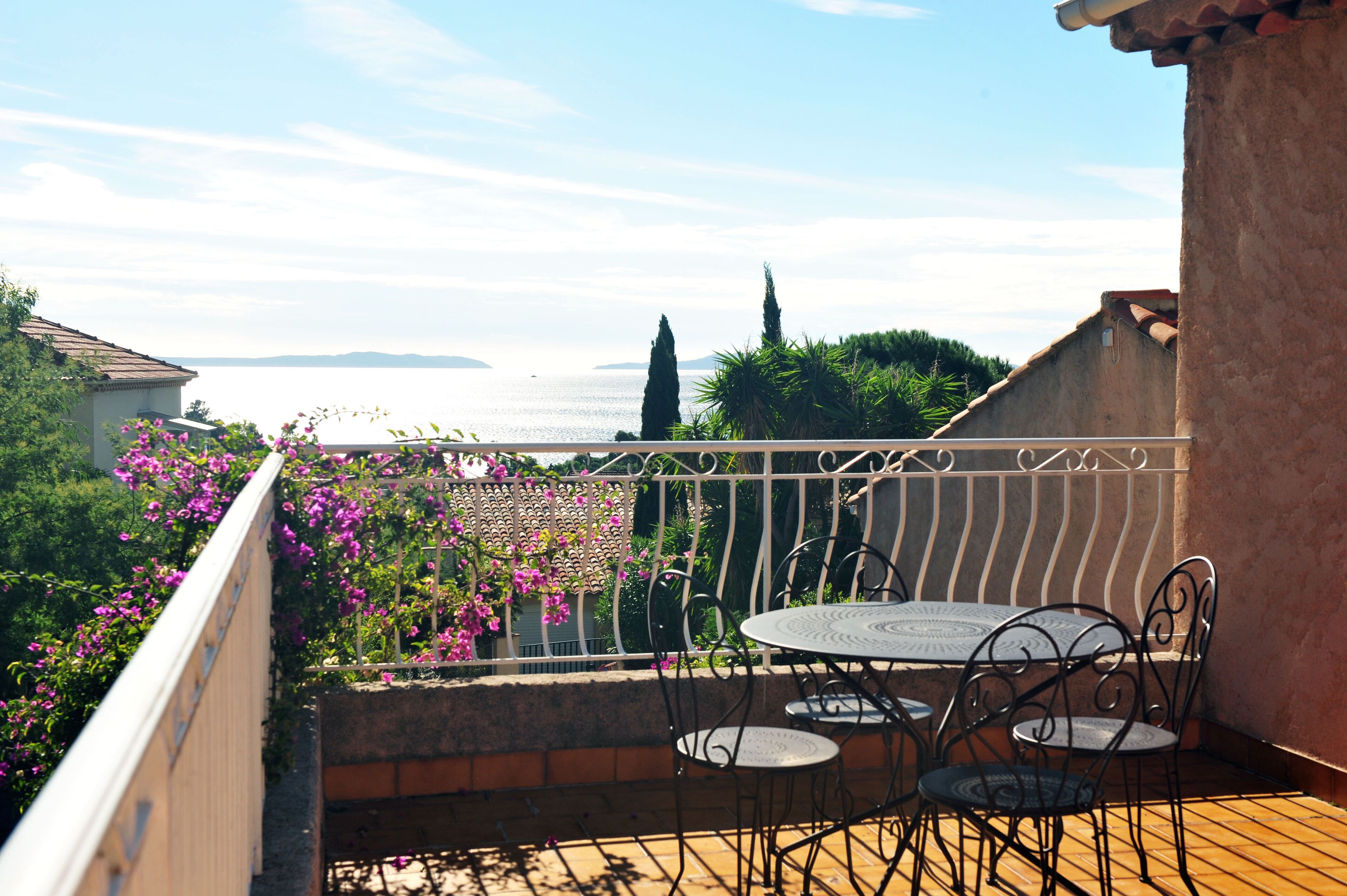 A balcony with a table and chairs, overlooking a body of water and distant hills.