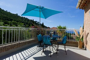 Une terrasse avec une table et des chaises, un grand parasol et une vue sur une colline.