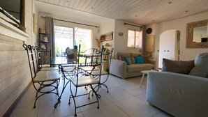 A living room with a sofa, a dining table with chairs, a window, and a door. - Charming sea view villa quiet close to the beaches (Le Lavandou)