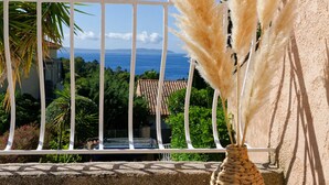 A balcony with a woven vase containing pampas grass, a railing, and a view of the sea and buildings. - Charming sea view villa quiet close to the beaches (Le Lavandou)
