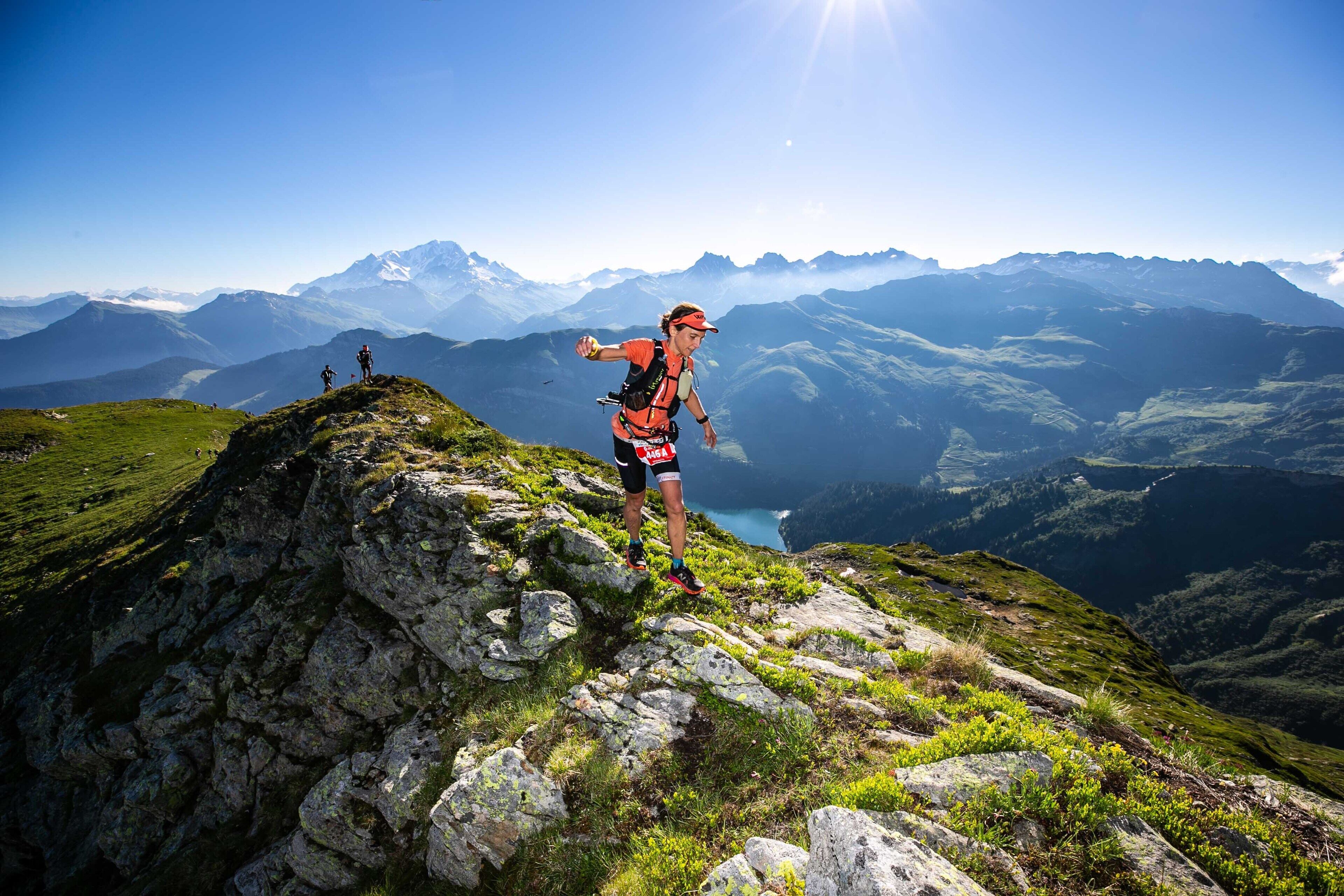 A person hiking on a mountain peak with a clear view of distant mountains and a valley below.