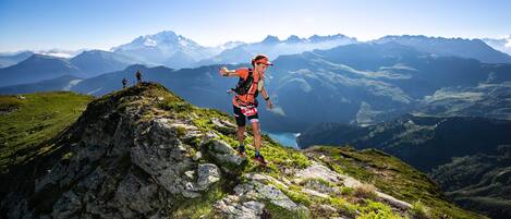 A person hiking on a mountain peak with a clear view of distant mountains and a valley below.
