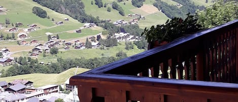 A wooden balcony railing overlooking a village with houses and green hills in the background.