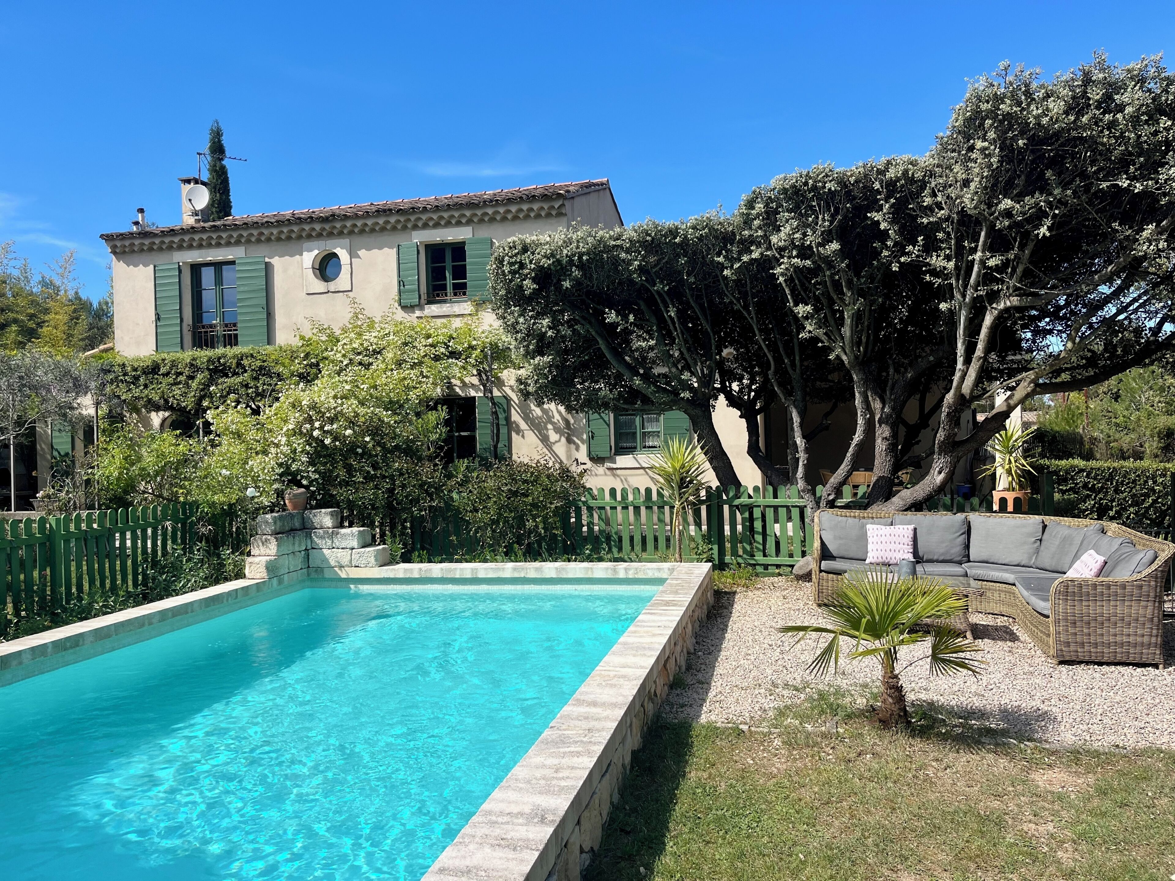 Une piscine, un canapé en osier et un bâtiment avec un toit en tuiles.