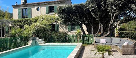 Une piscine, un canapé en osier et un bâtiment avec un toit en tuiles.