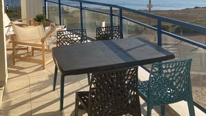 Een balkon met een tafel en stoelen, met uitzicht op een strand en de zee.
