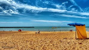 Een strand met een zandrijk strand, een blauwe en gele parasol, en een pier in de verte.
