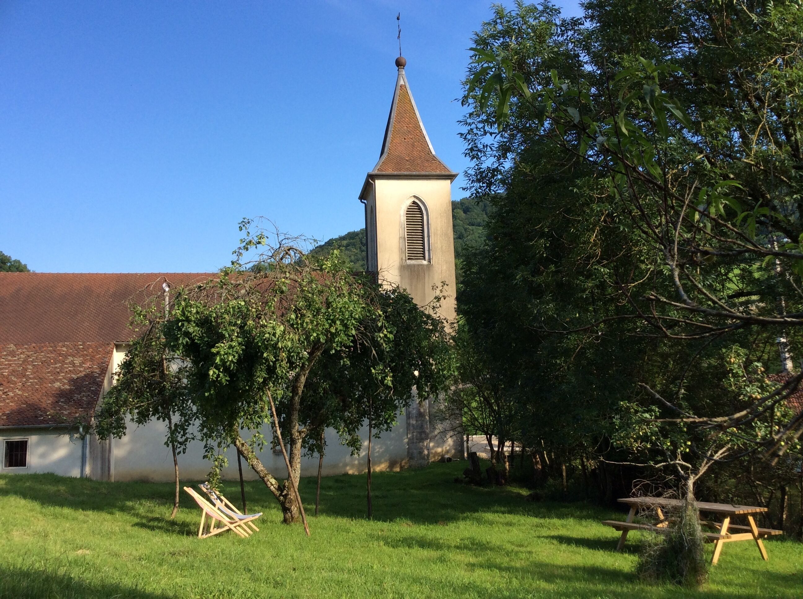 A church with a bell tower, surrounded by trees and a picnic table.
