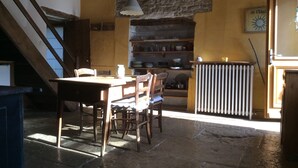 A rustic dining area with a wooden table and chairs, a stone wall, and a hanging light fixture.