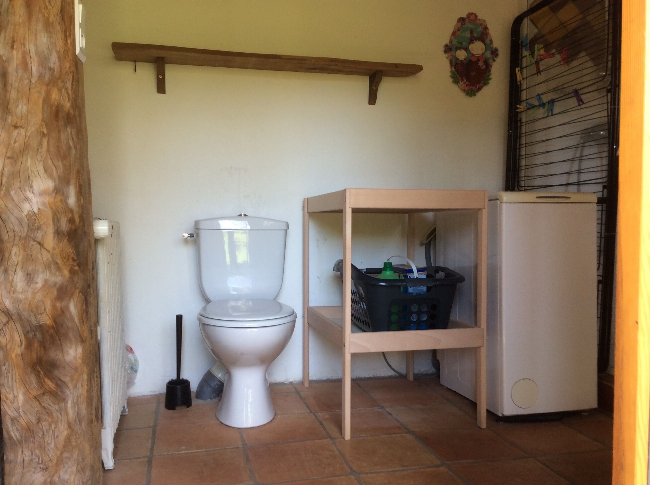 Et lille badeværelse med toilet, en træhylde med en kurv, en radiator og et køleskab.