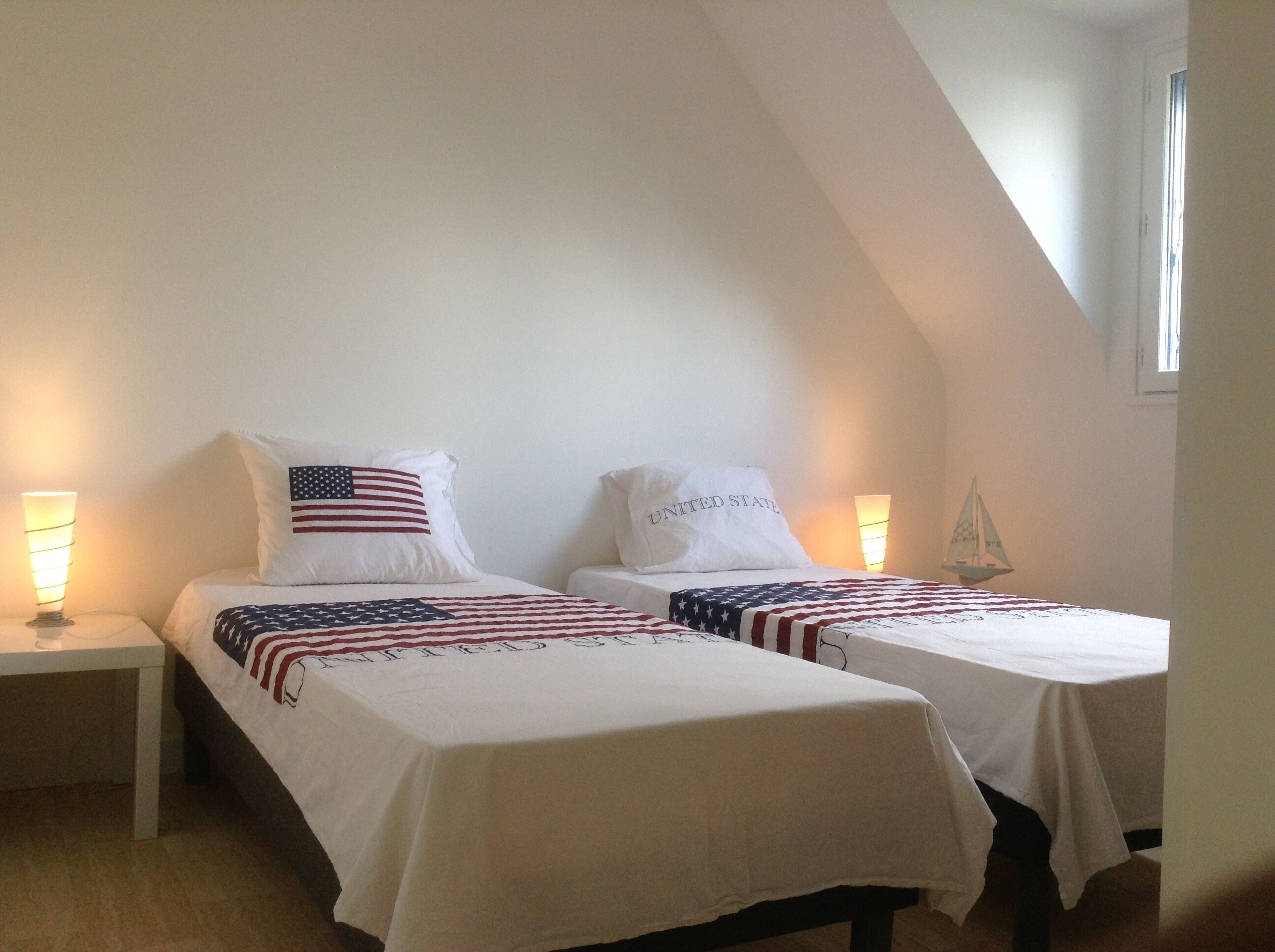 Un dormitorio con dos camas, cada una con una colcha y almohadas con motivos de la bandera estadounidense, y una decoración náutica de un velero en la pared.