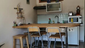 Uma cozinha compacta com ilha central, quatro cadeiras dobráveis, uma mesa pequena e um micro-ondas.