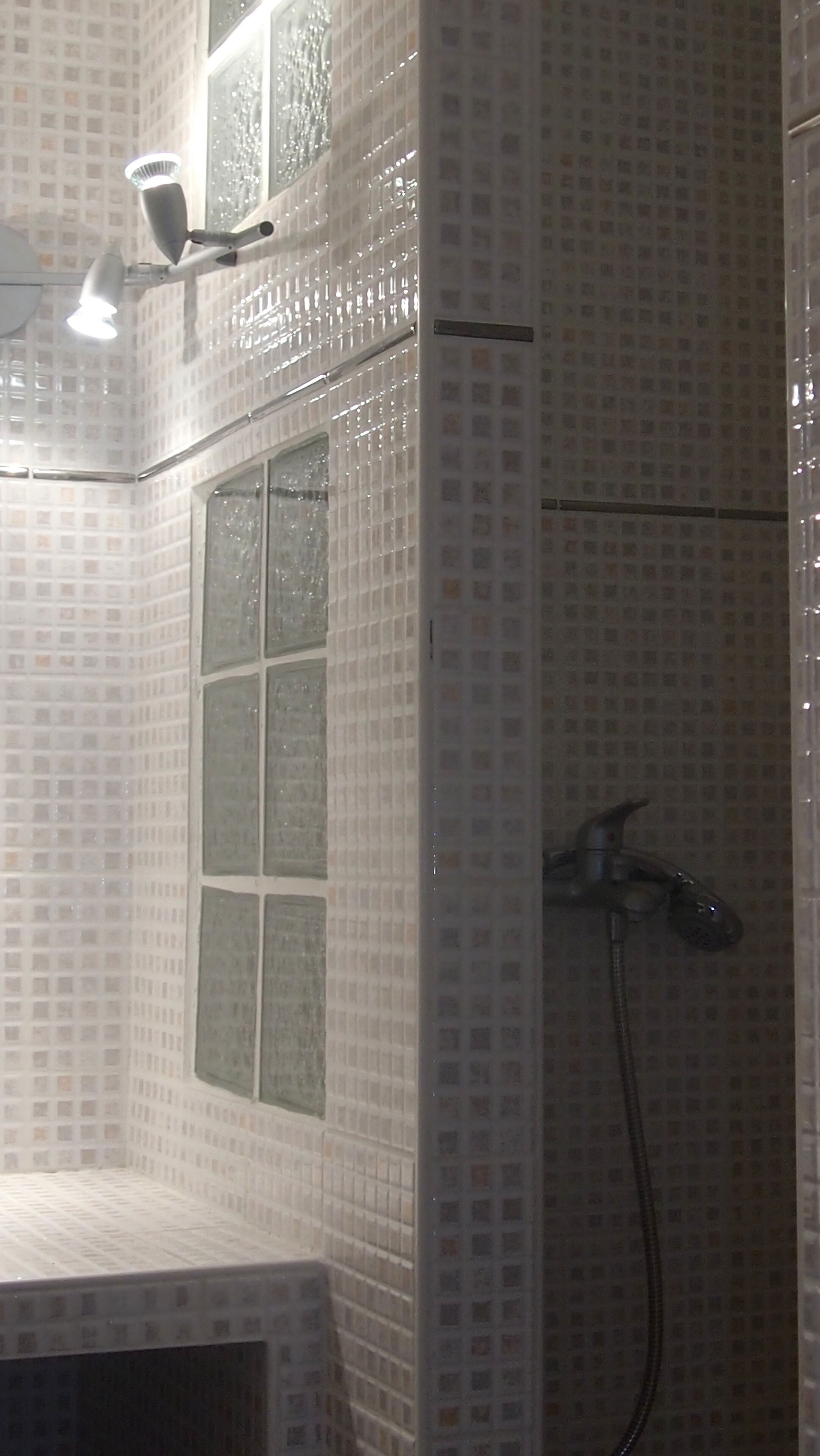 A bathroom with a tiled wall, a window, and a shower area.