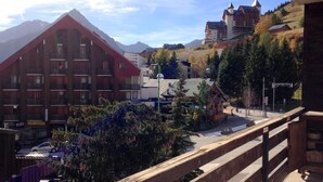 Um hotel com fachada vermelha, um chalé tradicional e montanhas ao fundo.