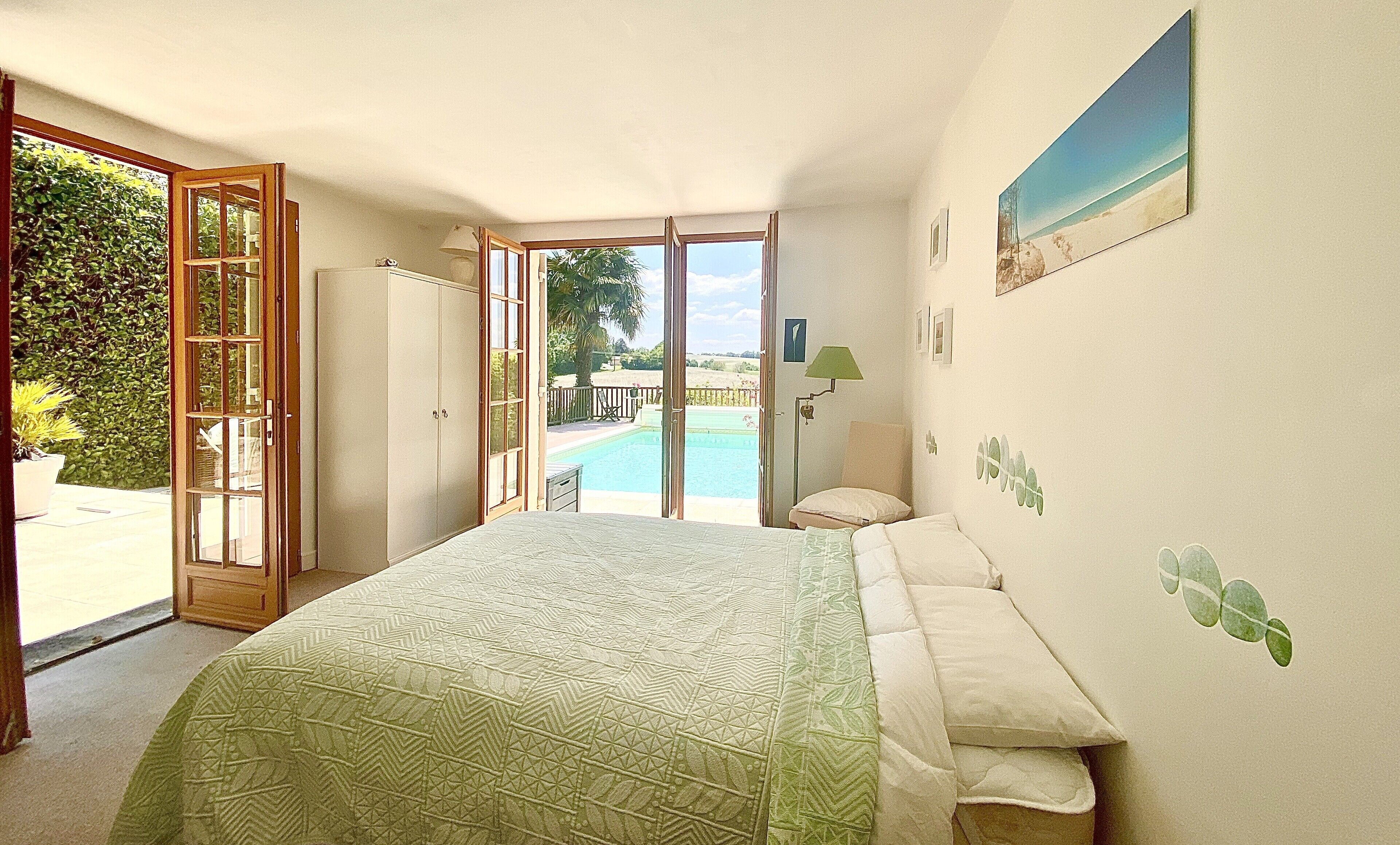 Un dormitori amb llit, vista a una piscina i una porta que dóna a l'exterior.