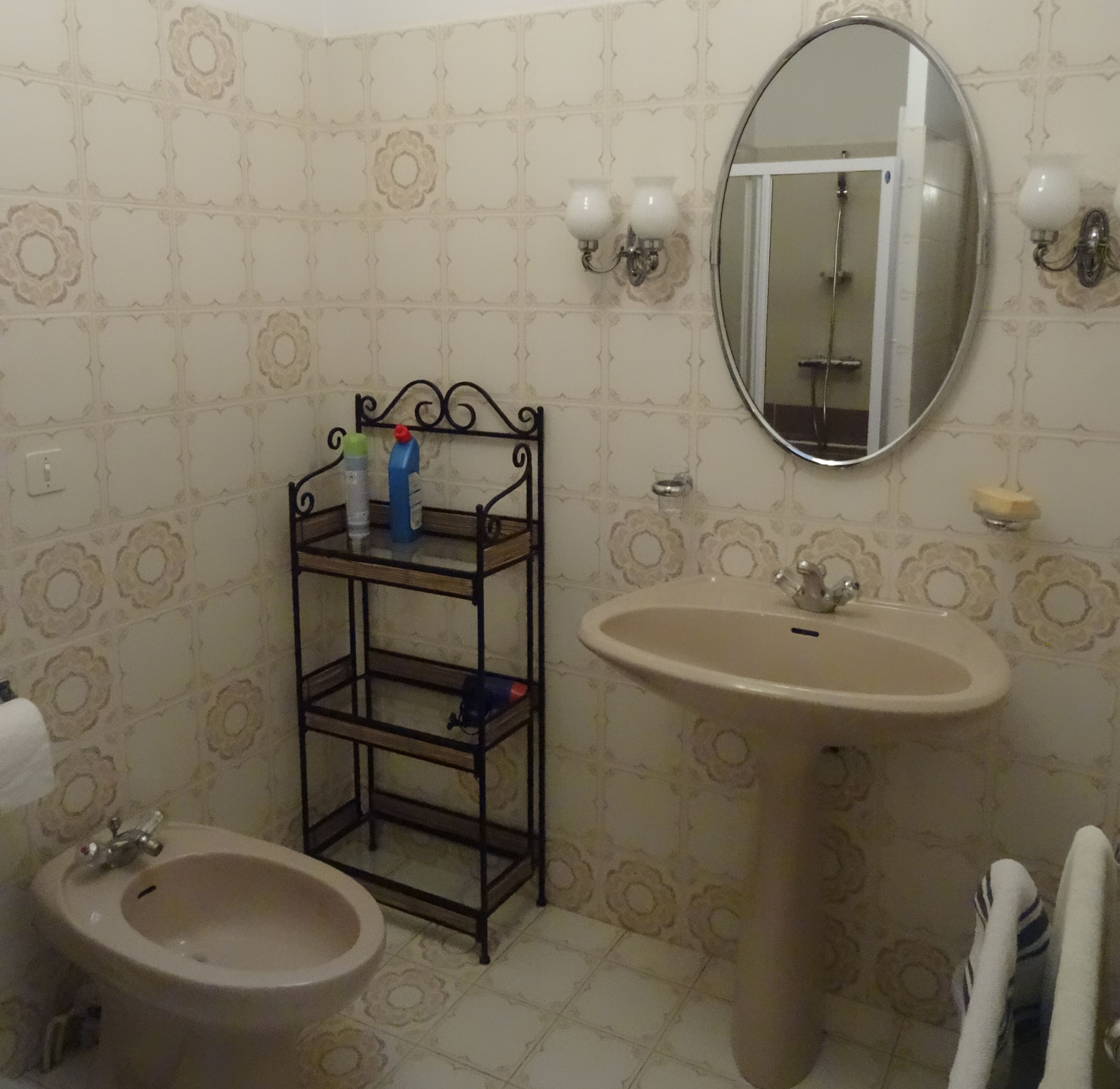 Un baño con lavamanos pedestal, un bidé, un espejo y estante con artículos de aseo.