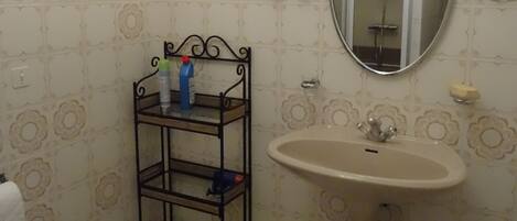 Un baño con lavamanos pedestal, un bidé, un espejo y estante con artículos de aseo.