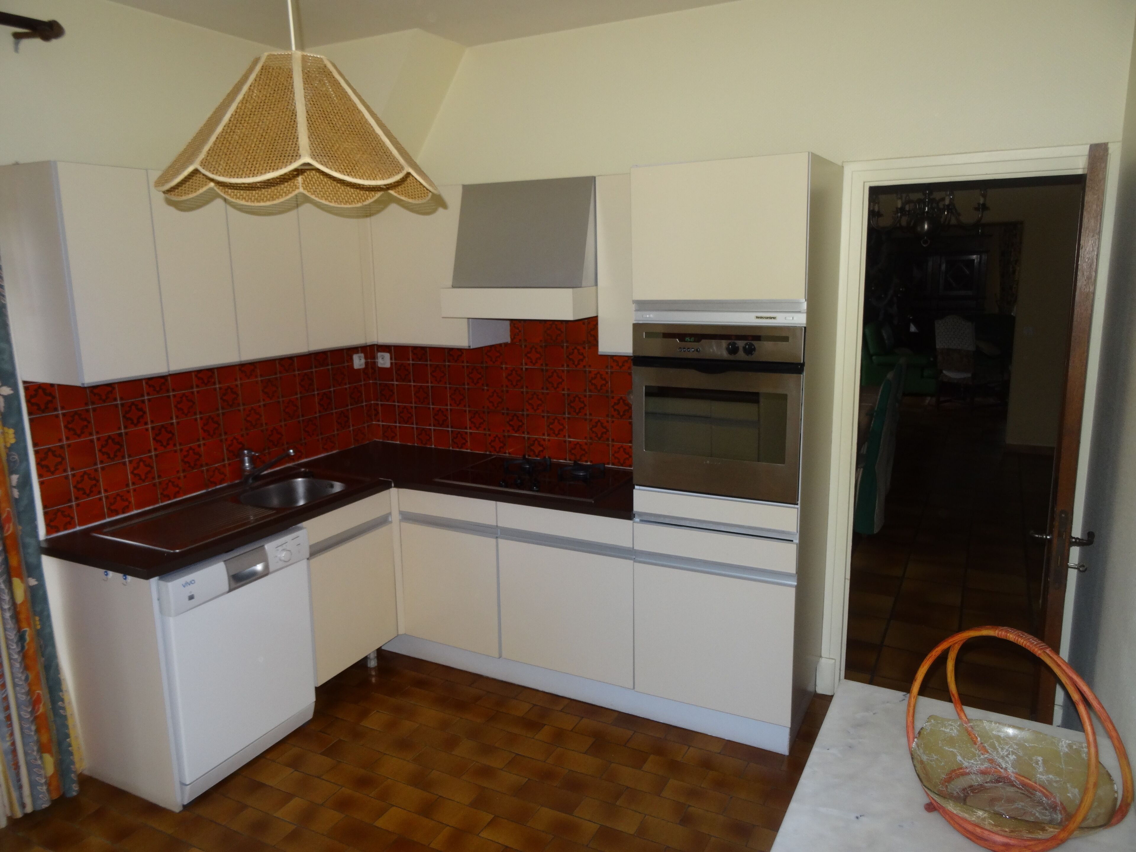 A kitchen with white cabinets, a red tiled backsplash, a stainless steel oven, and a hanging light fixture.