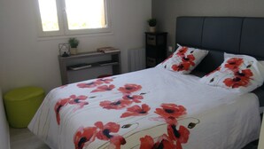 Ein Bett mit Blumenmuster, ein Nachttisch mit Lampe und ein Fenster mit Tageslicht.