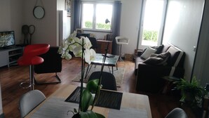 Ein modernes Wohnzimmer mit Essbereich, Fernseher und großem Fenster mit Vorhängen.