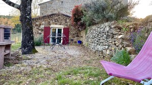 A stone building with a red door, a table with chairs, and a hammock in the foreground. - Sud Adèche in VINEZAC Cottage in the heart of an olive grove  (Vinezac)