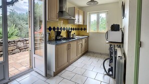 A kitchen with wooden cabinets, a gas stove, and a window overlooking a garden. - Sud Adèche in VINEZAC Cottage in the heart of an olive grove  (Vinezac)