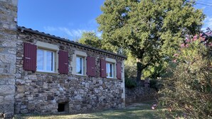 A stone building with red shutters, a small entrance, and a grassy yard. - Sud Adèche in VINEZAC Cottage in the heart of an olive grove  (Vinezac)