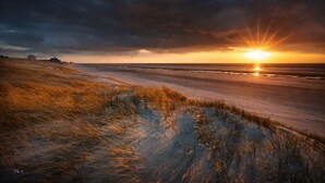 A beach at sunset with a dune in the foreground.