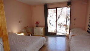 A bedroom with two beds, a wooden dresser, a chair, and a window with a view of a snowy landscape.