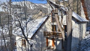 A snow-covered mountain house with a wooden balcony and a chimney.