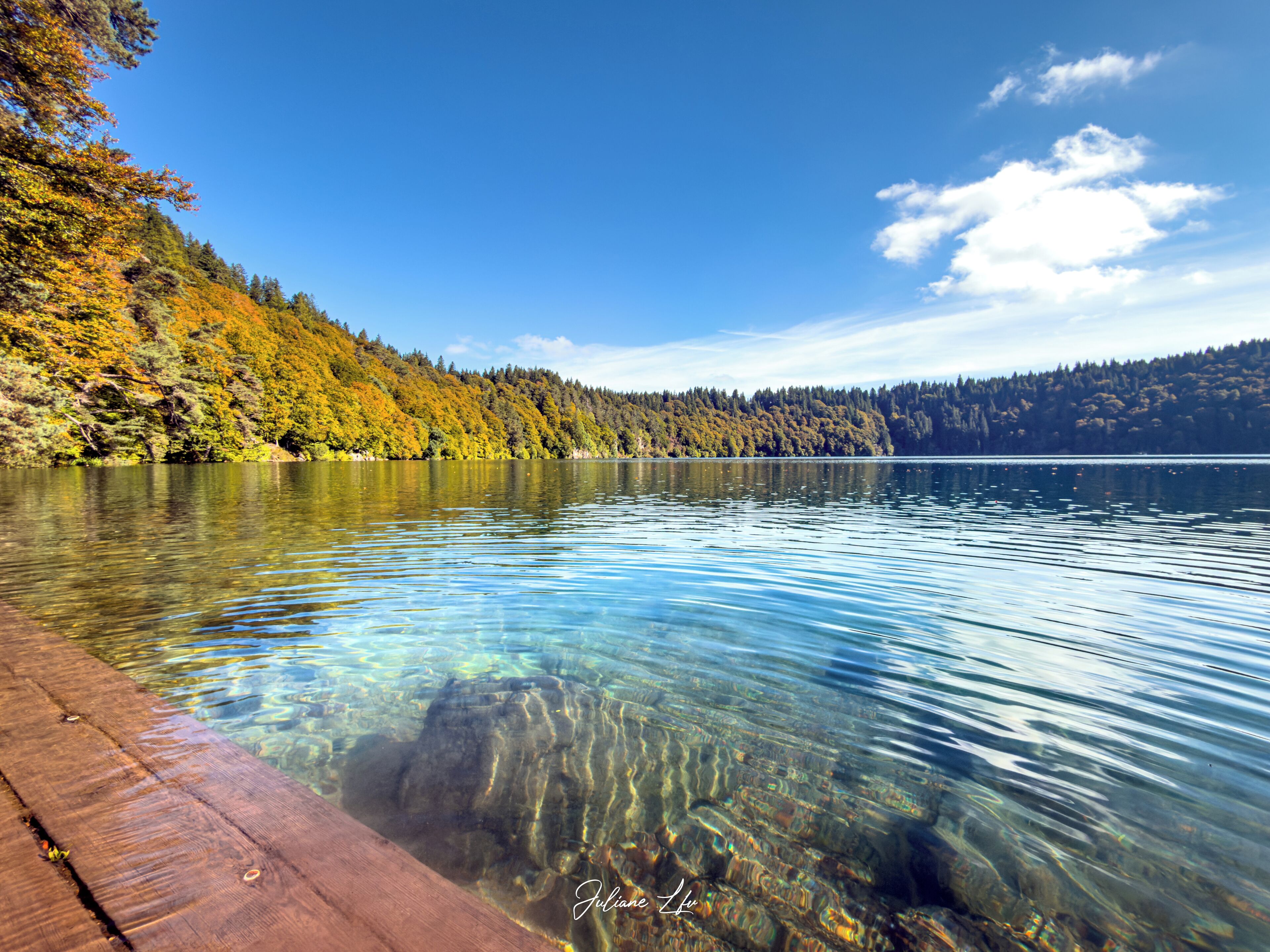 Un lago transparente con un muelle de madera que se adentra en el agua.