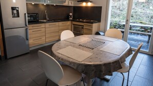 Eine moderne Küche mit integriertem Backofen, einer Mikrowelle und einer Kaffeemaschine. Ein Esstisch mit Stühlen und ein großes Fenster bieten einen Blick ins Freie.