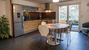 Eine moderne Küche mit Essbereich, ausgestattet mit einem Edelstahl-Kühlschrank, einer Mikrowelle, einem Herd und einem Esstisch mit Stühlen.