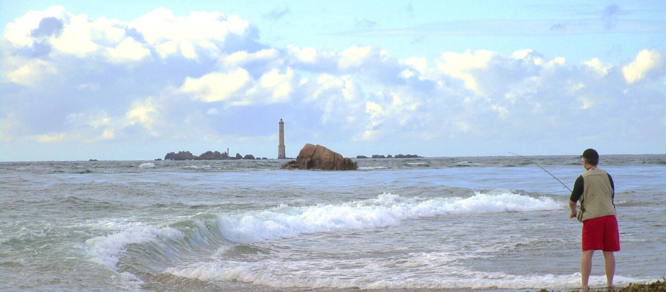 A person fishing by the sea with a lighthouse in the background.