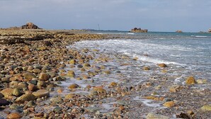 A rocky beach with waves crashing onto the shore, a lighthouse in the distance, and several rocky outcrops.