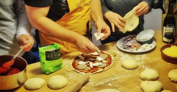 A group of people preparing food, specifically making pizza, with ingredients and utensils on a table.