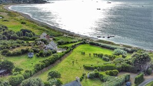 An aerial view of a coastal property with a stone building, green lawns, and a beach.