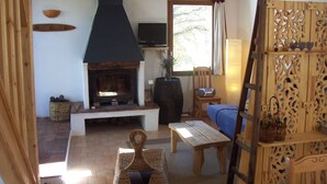 A cozy living room with a fireplace, a sofa, a wooden table, and a decorative wooden panel. - Brand new gite in an authentic Provencal Mas, in south Ventoux (Méthamis)