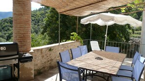 Une terrasse extérieure avec une table et des chaises, un barbecue et une vue sur une colline boisée.