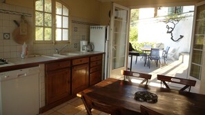 A kitchen with wooden cabinets, a sink, and a window. There is a dining table with chairs and a view of the outside. - A gite of character and grand comfort in the heart of nature (Saint-Laurent-Le-Minier)