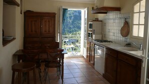 Une cuisine avec des meubles en bois, une table à manger avec des chaises, une vue à travers la porte ouverte et une fenêtre donnant sur l’extérieur.