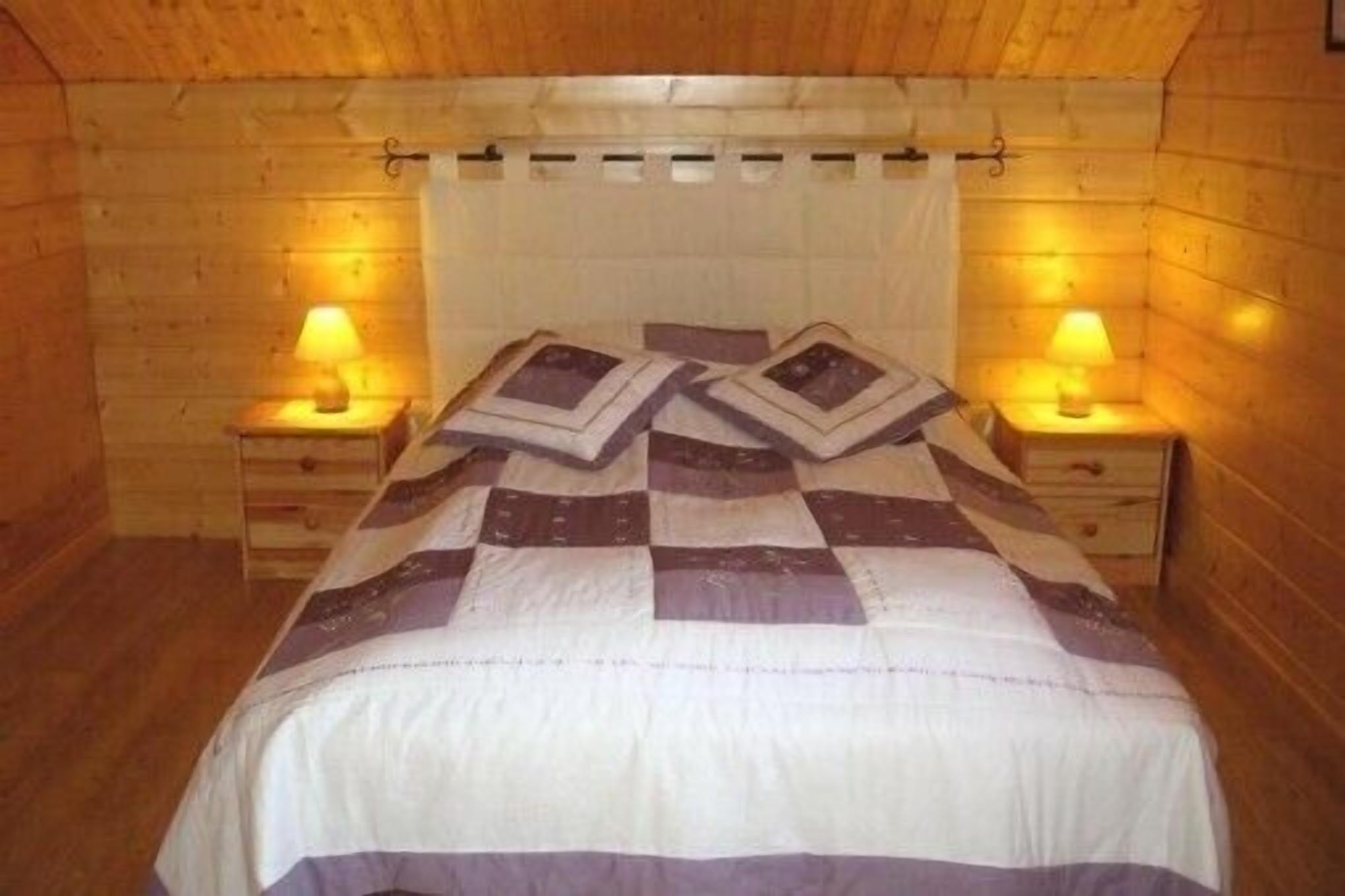 A wooden cabin room with a bed, two bedside tables, and a hanging light fixture.