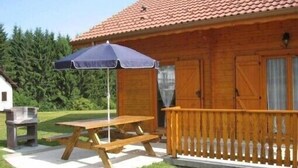 A wooden cabin with a picnic table and umbrella, surrounded by a wooden deck and a grassy yard. - Detached chalet 7 minutes away from Gerardmer (Le Tholy)