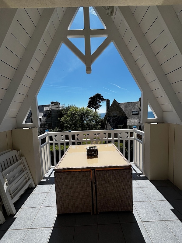 A covered balcony with a table and chairs, a view of the sea, and a white railing.