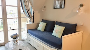 Een gezellige kamer met een bank, een klein tafeltje met een vaas, en uitzicht door een raam.