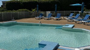 Zwembad met ligbedden en parasols, omringd door een hek en groen.