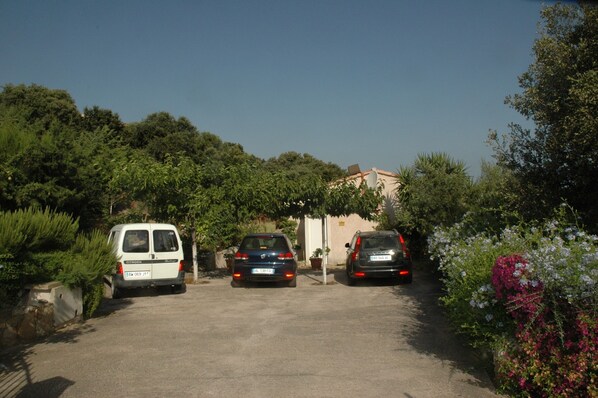 A parking area with three cars parked in front of a building surrounded by greenery. - air-conditioned T1 apartment for 2 people, terrace with sea view, garden & parking (Monticello)
